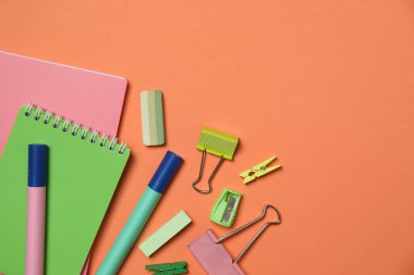 Turuncu arkaplan üzerinde not defterleri ve farklı kırtasiye malzemeleriyle düz konum, metin için boşluk