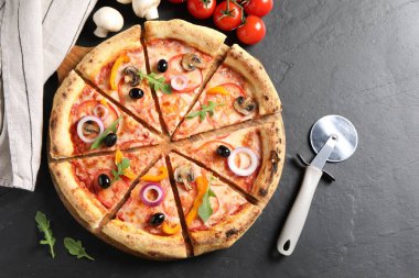 Lezzetli vejetaryen pizzası, kesme makinesi ve malzemeleri siyah masaya koyun.