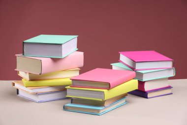 Pembe arka plana karşı bej masadaki birçok renkli kitap