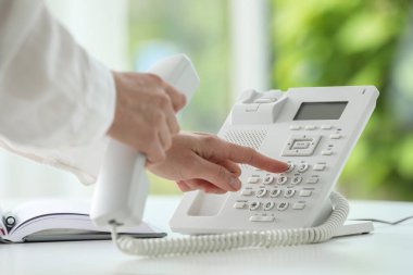 Assistant dialing number on telephone against blurred background, closeup