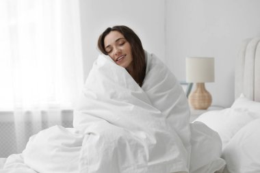 Battaniyeye sarılıp yatağa oturan mutlu kadın. Günaydın.