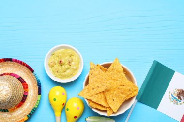 Meksika bayrağı, sombrero şapkası, marakas, cips ve açık mavi ahşap masa üzerinde guacamole. Metin için boşluk