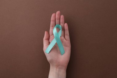 Kahverengi arka planda turkuaz farkındalık kurdelesi tutan kadın.