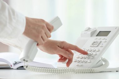 Assistant dialing number on telephone against blurred background, closeup