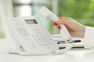 Assistant taking telephone handset at white table, closeup