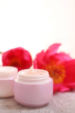 Kavanozlar dolusu krema ve şakayık çiçeği gri masada, arka planda ışığa karşı, yakın plan. Metin için boşluk