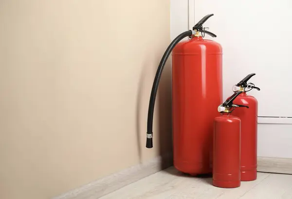 stock image Fire extinguishers on floor near beige wall indoors