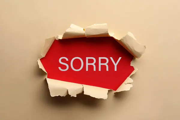 stock image Word Sorry on red background, view through torn beige paper