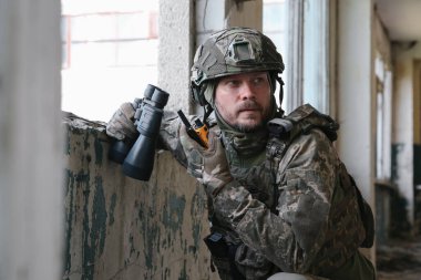 Military mission. Soldier in uniform with binoculars inside abandoned building