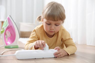 Little child playing with power strip and iron plug on floor indoors. Dangerous situation