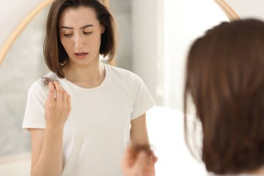 Stresli kadın içeride aynanın yanında saçlarını tutuyordu. Alopecia sorunu