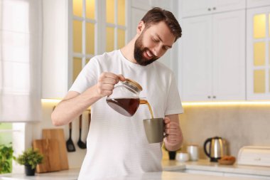 Mutlu genç adam sabah mutfakta fincana kahve dolduruyor.