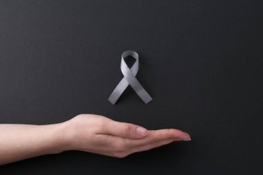 Siyah arka planda gri farkındalık kurdelesi olan kadın, üst görünüm