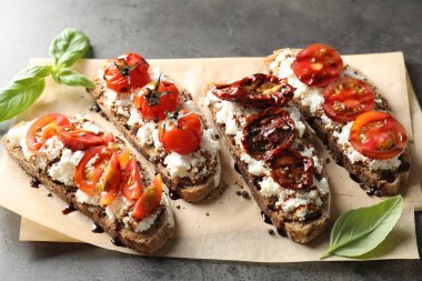 Lezzetli ricotta bruschettalar, güneşte kurutulmuş domatesler, sos ve fesleğen, gri desenli masalarda, üst tarafta.