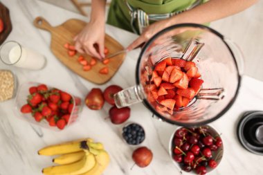 Mutfaktaki beyaz mermer masada blender ile nefis smoothie yapan kadın.