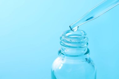 Açık mavi arka planda pipetten cam şişeye sıvı damlatıyor, yakın plan. Metin için boşluk