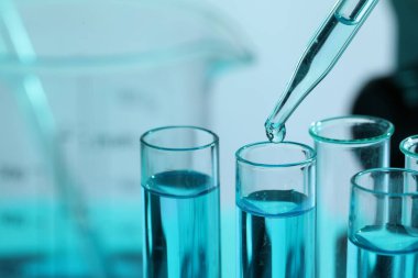 Bulanık arka planda pipetten test tüpüne sıvı damlatılıyor. Yakın plan. Metin için boşluk