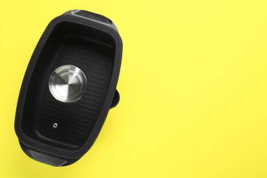 Sarı arka planda cam kapaklı siyah tencere, üst manzara. Metin için boşluk