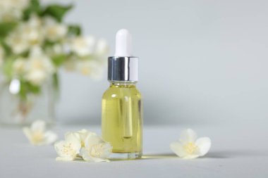 Şişedeki temel yağ ve gri arka planda güzel yasemin çiçekleri, yakın plan.