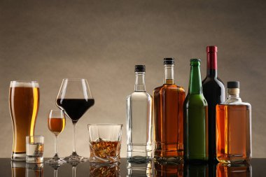 Bej arka planda farklı alkollü içeceklerle dolu şişeler ve bardaklar