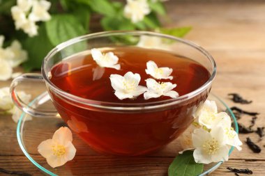 Sıcak yasemin çayı fincanda ve çiçekler ahşap masada, yakın plan.