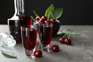 Şat bardaklarında kiraz likörü, sürahi ve gri masada taze böğürtlen.