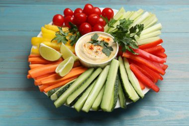 Lezzetli ev yapımı humus ve açık mavi ahşap masada servis edilen farklı sebzeler.