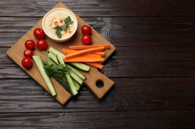 Lezzetli ev yapımı humus ve koyu ahşap masa üzerinde farklı sebzeler.