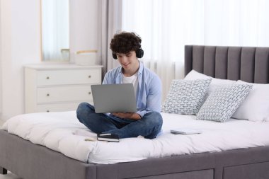 Evde dizüstü bilgisayarla çalışan kulaklıklı bir genç. Uzak görev