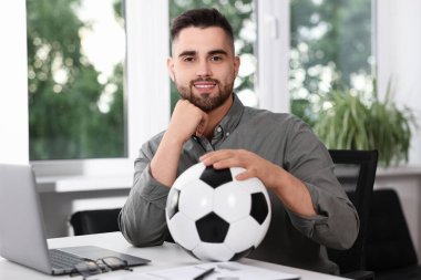 Masasında futbol topu olan genç bir adam.