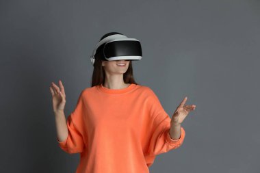 Gülümseyen kadın gri arka planda sanal gerçeklik kulaklığı kullanıyor.