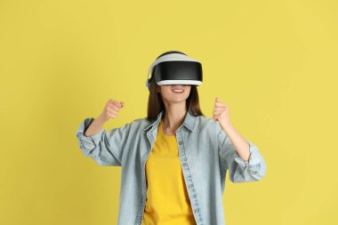 Gülümseyen kadın sarı arka planda sanal gerçeklik kulaklığı kullanıyor.