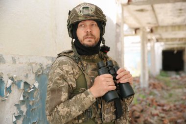 Military mission. Soldier in uniform with binoculars inside abandoned building