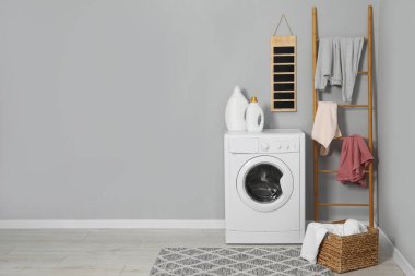 Çamaşır makinesi, deterjan, merdiven, sepet ve çamaşırhane kapalı alanda gri duvar, metin için yer