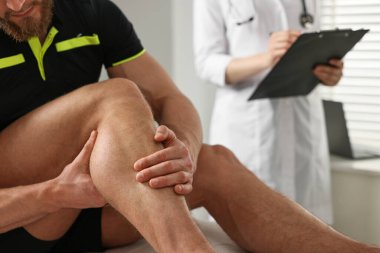 Doktorlar hastanede belgeleri doldururken sporcu bacağını tutuyor.