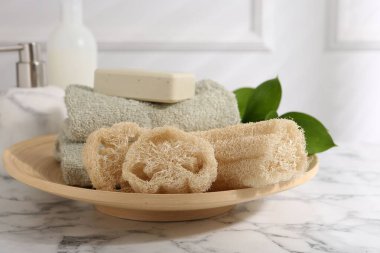 Lif süngeri, sabun, havlu ve yeşil yapraklar beyaz mermer masa üzerinde.