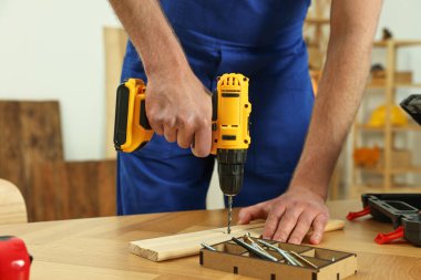 Zanaatkar atölyedeki ahşap masada matkapla çalışıyor.