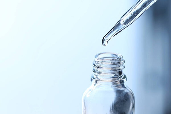 Dripping liquid from pipette into glass bottle on light blue background, closeup. Space for text