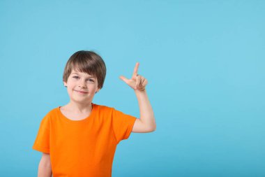 Sevimli küçük çocuk açık mavi arka plandaki bir şeyi işaret ediyor, mesaj için boşluk.