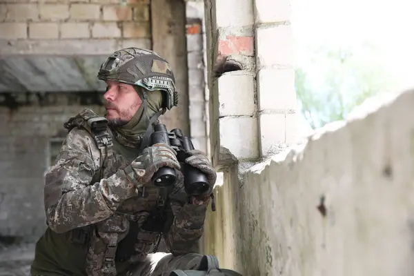 stock image Military mission. Soldier in uniform with binoculars inside abandoned building, space for text