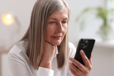 Evde cep telefonu kullanan yaşlı bir kadın.