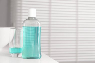 Banyodaki beyaz tezgahta şişe ve bardak gargara. Mesaj için yer var.