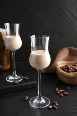 Bardakta kremalı kahve likörü ve siyah ahşap masada fasulye.