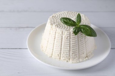 Taze ricotta (krem peynir) ve fesleğen beyaz ahşap masada.