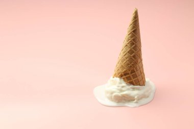 Açık pembe arka planda wafer külahında erimiş dondurma. Metin için boşluk