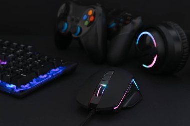 Bilgisayar faresi, kulaklık, RGB klavye ve oyun denetleyicileri siyah arkaplanda, yakın plan