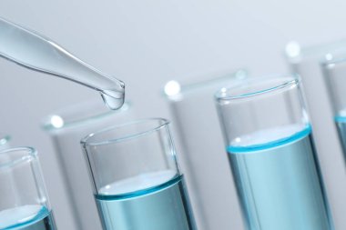 Işık arka planında pipetten test tüpüne sıvı damlatılıyor, yakın plan