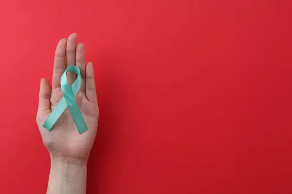 stock image Woman holding turquoise awareness ribbon on red background, top view. Space for text