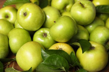 Fresh ripe green apples with leaves on wooden table, closeup