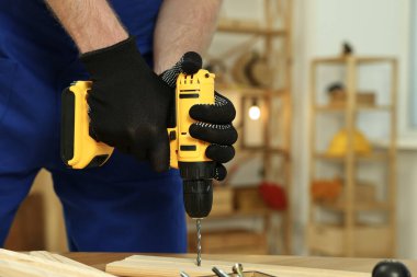 Zanaatkar atölyedeki ahşap masada matkapla çalışıyor, yakın plan. Metin için boşluk